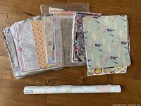 Multiple wallpaper sheets with assorted 1980s style patterns laid out on a wooden floor, showing floral, abstract, and umbrella prints.