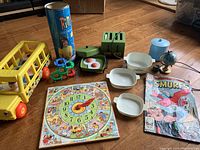 Full lot overview on wood floor showing all toys, dishes, comic, and puzzle.