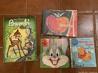 Four vintage children's books laid flat: Walt Disney Bambi, Brian Wildsmith ABC, Bugs Bunny, and Winnie the Pooh The Honey Tree.