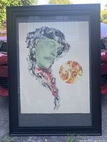 Frontal photo of the framed silkscreen art showing the green portrait with black, red details and an orange circular shape on rag paper under glass.