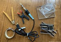 Overview image showing all items on a wooden surface: soldering iron, clamps, coil of lead coming, and plastic sheets.