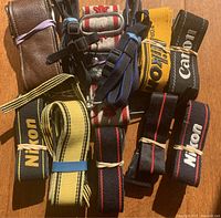Top view showing assorted camera straps including Nikon yellow and black, Canon black, brown leather strap, and blue and beige patterned straps, rubber-banded together