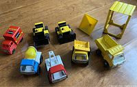 Eight pressed steel vintage toy trucks and yellow plastic accessories arranged on a surface