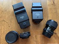 Two Vivitar electronic flash units and three related camera lenses/parts displayed on wood surface.
