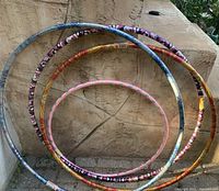 Five colorful Wave hula hoops leaning against a textured wall outdoors, showing size variation from small to large.
