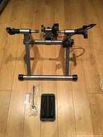 Side view of indoor bike trainer frame positioned on wood floor with included accessories laid out, showing metal construction and magnetic resistance unit.