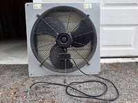 Front view of fan motor with black blades and protective grille visible, metal fan housing square shaped, pull cord hanging down attached to motor box.