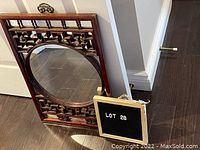 Frontal view of the wooden framed circular mirror showing Asian-inspired geometric pattern and wooden carved details on top and bottom of the rectangular frame, with wear visible on the wood.