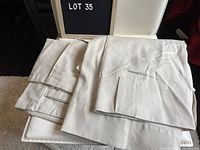 Two beige panel curtains folded and displayed on a white surface, showing fabric texture and tab tops.