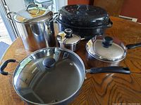 Top view showing all five cookware pieces grouped together on a wooden table: 6" saucepan, 8.5" pot, 9.25" soup pot, 12" chicken pan, 15.5x11.5" roasting pan with lids.