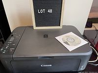 Photo of Canon Pixma MG2100 scanner with original disk on top showing the device and disk in detail.