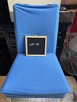 Front view of a blue slip cover fitted on a dining chair with a black sign displaying 'LOT 47'.