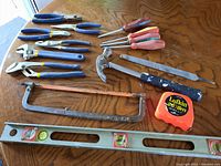 Overview of tools laid out on wooden surface showing hammer, hacksaw, measuring tape, file, level, and screwdrivers.