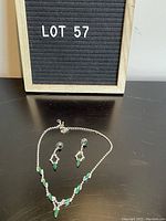 Photo of vintage green rhinestone necklace and earrings set against black background with labeled lot number