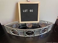 Curved metal votive holder with three cylindrical purple-tinted glass holders mounted inside circular metal frames.