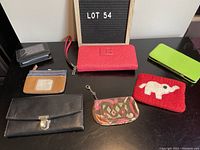 Photo showing seven assorted wallets and coin purses on a black surface with a sign reading LOT 54 behind.