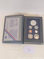 Open presentation case with seven proof coins arranged in blue felt insert along with certificate of authenticity visible.
