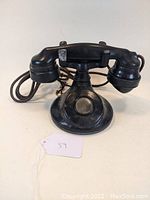 Front view of antique Western Electric black Bakelite candlestick-style telephone, showing mouthpiece, round base, and earpiece with attached cord.