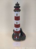 Full view of the painted lighthouse figurine with attached buildings and base, showing red and white stripes and detailed small buildings at the bottom.
