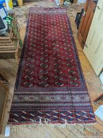 Full-length view of red runner rug on wooden floor showing repeating Bokhara pattern