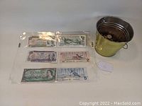 Four vintage Canadian banknotes arranged flat with a small metal bucket containing coins on the side.