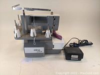 Elna Lock serger sewing machine front and left side view with threading system and power adapter visible.
