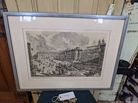 Full front view of the framed print propped on a chair seen in a workshop setting with a close view of the surrounding mat and frame.