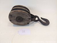 Side view of wooden block and tackle pulley showing three wooden sheaves and iron hook.