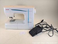 Janome Xpression sewing machine with black foot pedal and cable placed beside it on a white surface.