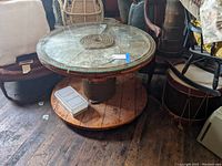 Full view of the large wooden spool table with glass top and jute rope wrapping, sitting among other furniture on a wooden floor.