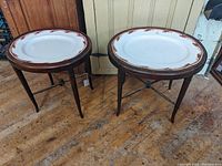 Two oval porcelain platters set into round wooden tripod display stands on wooden floor