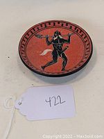 Photo of redware ceramic dish featuring a black masked figure holding a spear, geometric border visible