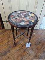 Full view of the side table showing the mosaic stone top and wooden frame with turned legs.