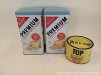 Two Nabisco Premium Saltine Crackers tins and one Top Cigarette Tobacco tin displayed together, showing front and top views.