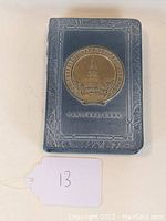 Front view of the locking book bank showing blue textured cover and brass embossed medallion with Travelers Bank and Trust Company logo, Hartford, Conn.