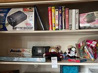 Shelf showing CyberPower battery backup UPS box, Atari Linx hand held console, paint-by-number kit, dolls, and miscellaneous toy packages.