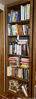 Full view of wooden bookshelf filled with multiple rows of books of varying thickness and color.