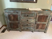 Front view of rustic wooden kitchen cabinet showing three drawers in the middle and two doors with metal panels on each side.