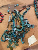 Photo showing a collection of gemstone and glass bead necklaces, earrings on dauplaise cards, and bracelets in a cluster on a wooden surface.