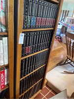 Wooden bookshelf shelf with Encyclopaedia Britannica volumes, including a red-spined 1996 edition among black spines with gold lettering
