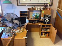 Wide desk view showing two fans, monitor, decorative items, lamp box and office supplies