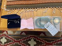 Wide view of all jewelry items arranged on a wooden surface, showing turquoise bead bracelets, set of silver jewelry in a Montana Goldsmiths case, silver floral earrings, and silver rings and bracelets.