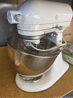 White KitchenAid Ultra Power stand mixer with stainless steel mixing bowl and plastic pouring shield, placed on wooden surface, showing front and side view