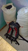 Two beige canvas stuff sacks printed with red Marmot logo standing upright with a North Face backpack in front