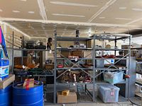 Wide view of three large grey metal shelving units in garage with various household items stored on shelves.