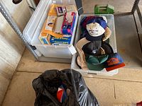Two clear plastic totes side by side on concrete floor, one with envelopes and one with hats