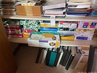Shelf stacked with many reams of printer paper in different brands and packages, along with boxes of envelopes and some binders below.