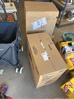 Two cardboard boxes, one Bounty paper towel box and one Seventh Generation brown bath tissue box, placed on a garage floor.