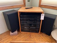 Full view of Pioneer stereo system in wooden cabinet with two speakers and remote on top.
