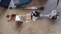 Overall view of string trimmer with accessories laid on concrete floor
